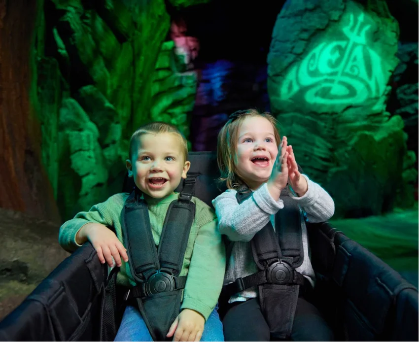 Two children seated in a WonderFold stroller wagon with five-point harnesses